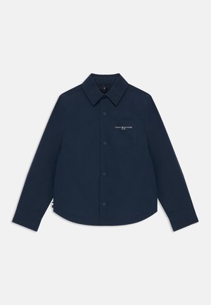 Camicia blu navy con bottoni in tessuto leggero. Presenta un colletto classico, taschino frontale con logo e un orlo curvo. Maniche lunghe.