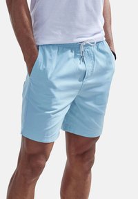 Light blue swim shorts made of soft fabric with an elastic waistband, drawstring closure, and side pockets. Simple design with no patterns.