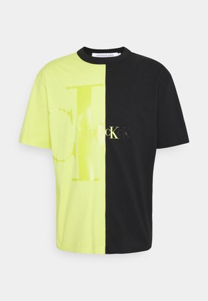 T-shirt à manches courtes avec un design divisé : un côté jaune vif avec un grand logo, l'autre côté noir uni. Tissu en coton.