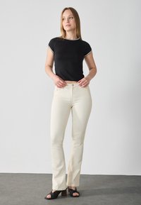 Black short-sleeve top with white trim paired with light beige fitted jeans. Material appears smooth; jeans have a button closure and pockets.