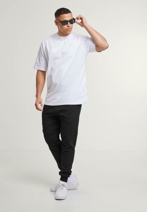 Hvit kortermet t-skjorte kombinert med svarte joggebukser og hvite sneakers, stående posisjon, iført svarte solbriller, glatte teksturer.