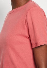 T-shirt med kort ärm och rund hals i korallrosa, tillverkad av mjukt tyg med en slät textur, med subtila sömnadsdetaljer.