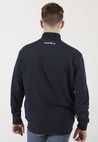 Pull-over en polaire marine avec col haut, fermeture éclair et logo brodé au dos. Présente un ajustement décontracté et un tissu texturé.
