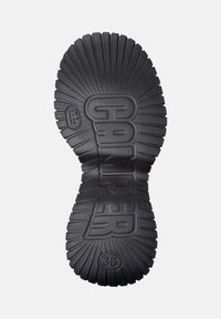 Suela de zapato de goma negra con textura estriada y un diseño acampanado. Presenta las palabras "CAMPER" y la talla "38" en relieve en la superficie.