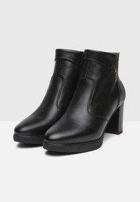 Bottines en cuir noir avec un bout pointu et un talon bloc. Présente des détails cousus et un bouton sur le côté pour le design. Texture lisse.