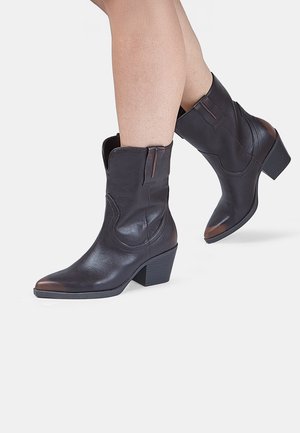 Brown leather ankle boots with a pointed toe, slight heel, decorative stitching, and pull tabs on the sides. Smooth texture and sleek design.