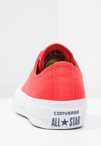 Red canvas sneaker with a low-top design, white rubber sole, and "Converse All Star" branding on the side. Textured surface.