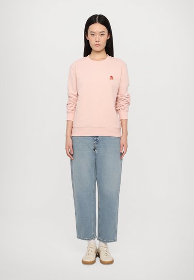 Lyserød sweatshirt med ribbede manchetter og kant, præsenterer et lille rødt logo. Sammen med lyseblå, løstsiddende jeans og beige sneakers.