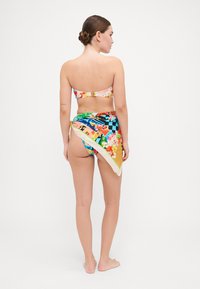 Conjunto de bikini con estampado floral en tonos rosa y azul, acompañado de un pareo multicolor con patrones audaces y un acabado satinado.
