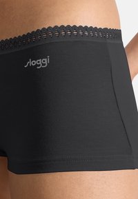 Svarta Sloggi boyshorts med vågformad spetsmidja och slät tyg. Sidoseamsdetalj, inga synliga etiketter eller metallbeslag.