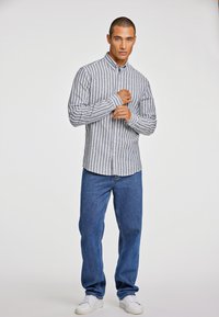 Camicia a righe in grigio chiaro e bianco, realizzata in un mix di cotone, abbinata a jeans blu e sneaker bianche. Maniche lunghe, colletto classico.