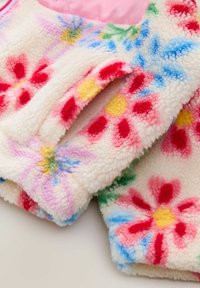 Giacca in pile morbido con motivi floreali multicolori in rosa, rosso, giallo e blu su sfondo crema. Finitura morbida e texturizzata.