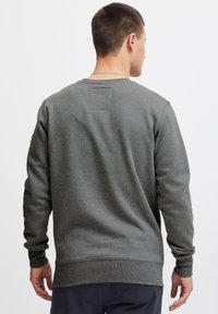 Sudadera gris con cuello redondo, mangas largas y puños acanalados. Presenta un pequeño parche de tela en la parte superior de la espalda y una textura suave.