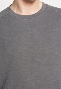 Sudadera gris de cuello redondo en una suave mezcla de algodón, que presenta una textura sutil y costuras reforzadas a lo largo de las costuras. Diseño ligero.