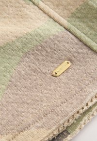 Tissu en maille douce avec des rayures beige, vertes et taupe, comportant une petite étiquette métallique dorée gravée "DOWNTHREE."