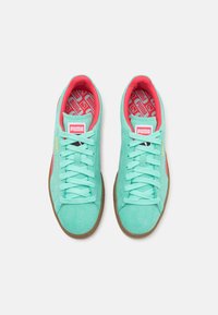 Paire de baskets Puma turquoise avec semelles en gomme, doublure intérieure corail et logo Puma blanc sur la languette, vue de dessus sur fond blanc.