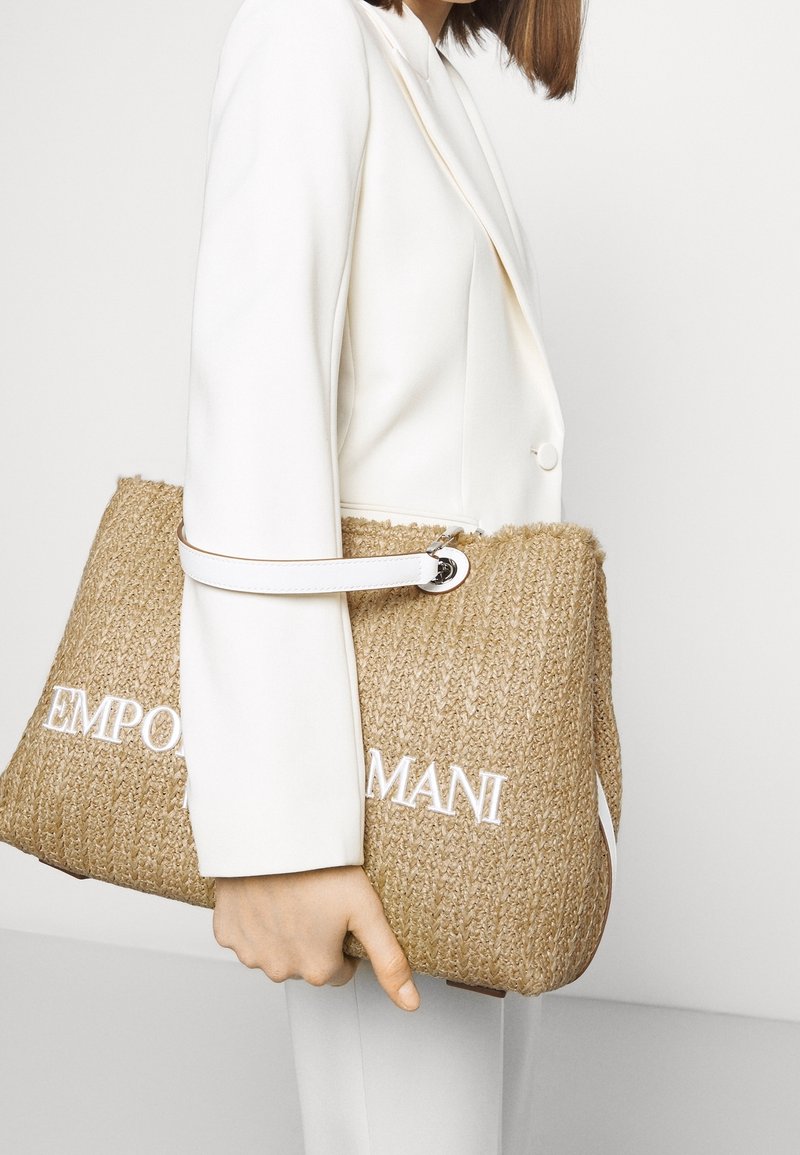 Vävd halmhandväska med vitt broderat "EMPORIO ARMANI"-logotyp, med ett slätt vitt handtag och rektangulär form.