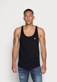 Svart tanktopp laget av bomull med rund halsutskjæring. Har et lite, hvitt broderi av logoen på brystet. Brukt sammen med blå, slitte jeans.