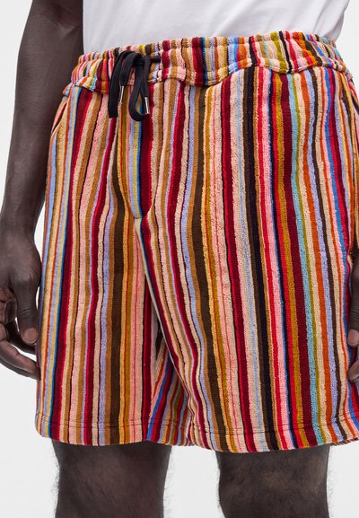 Gros plan d'une personne portant un short en éponge rayé coloré avec une taille élastique noire à cordon, sur un fond blanc uni.