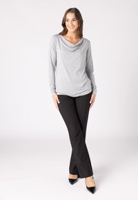 Grauer Langarmshirt mit drapierter Halslinie, kombiniert mit schwarzen, eng anliegenden Hosen und schwarzen spitzen Heels. Schlichtes Design, glattes Material.