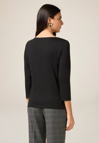 Sort, tætsiddende top med trekvartærmer og bred halsudskæring. Glat tekstur. Båret med grå ternede højtaljede bukser.