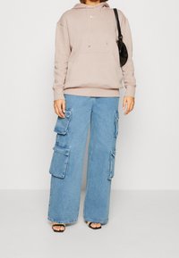 Felpa con cappuccio rosa chiaro, dotata di tasca frontale e cordini, abbinata a pantaloni cargo in denim blu a gamba larga con diverse tasche.