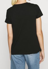 Musta puuvillainen t-paita, jossa on klassinen pyöreä kaula-aukko ja lyhyet hihat. Selkäosa on sileä ja malli on rento, yhdistettynä vaaleansinihin farkkuihin.