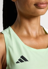 Top deportivo sin mangas de color verde claro, fabricado en material de malla. Presenta un escote redondeado y un logo de Adidas en negro en el lado izquierdo.