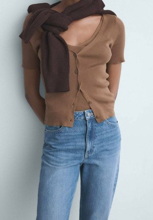 Cardigan scurt cu mâneci scurte, în nuanță de maro, cu dungi, purtat peste un top maro cu decolteu în V, asortat cu blugi denim decolorat, cu talie înaltă. Texturi moi și design ajustat.