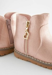Rosenvergoldete Wildleder-Ankelstiefel mit einem seitlichen Reißverschluss, der einen herzförmigen Zipper hat, Gummisohle und dekorativen Nähten entlang der Kanten.
