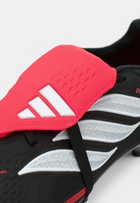 Μαύρο ποδοσφαιρικό παπούτσι με υφή κόκκινη επικάλυψη, διαθέτοντας λευκές ρίγες και αξεσουάρ. Σόλα σχεδιασμένη για τεχνητό γρασίδι.