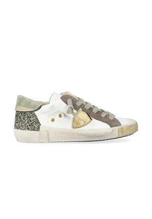 Sneaker bassa bianca con lacci grigi, dettagli in suede marrone, logo a scudo dorato, tallone glitter verde e suola logorata.