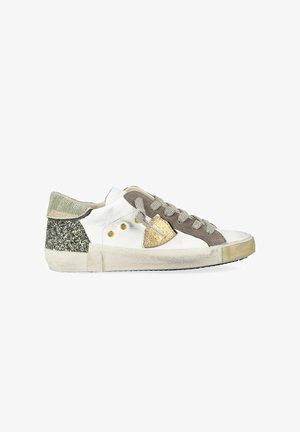 Witte lage sneaker met grijze veters, bruine suède accenten, gouden schildlogo, groene glinsterhiel en versleten zooldetails.