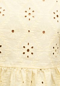 Tissu crème avec motifs floraux brodés présentant de petites découpes au centre des fleurs et des détails de bord festonnés.