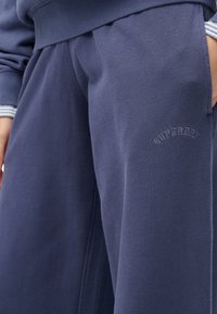 Pantalones de chándal azul marino fabricados en un tejido suave, con cintura elástica, bolsillos laterales y un pequeño logo bordado de "Superdry".