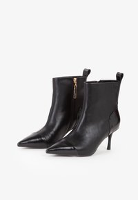 Stivali ankle in pelle nera con punte appuntite, tacchi sottili, zip laterale e cerniere, esposti su uno sfondo bianco.