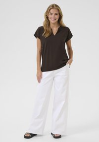 Brown v-neck t-shirt with short sleeves, paired with white wide-leg pants and black sandals featuring gold hardware accents. Simple, casual look.