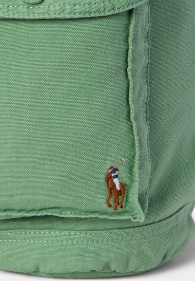 Πράσινο ύφασμα με λεπτομερή ραφή και μικρό κεντημένο λογότυπο παίκτη πόλο επάνω σε άλογο κοντά στην κάτω γωνία.