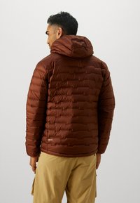 Brown insulated jacket with a hood, featuring a quilted design and smooth texture. Logo detail visible near the hem.