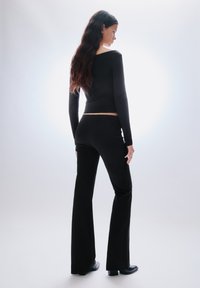 Fekete hosszú ujjú felső és bővülő nadrágok, sima anyagból készült. A felső rövidített, négyzet alakú nyakkivágással. Vékony szabású.