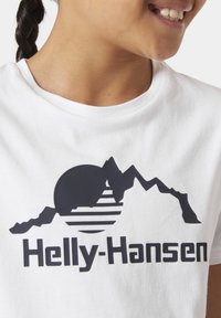 Camiseta blanca con un diseño gráfico negro que muestra montañas y un sol. Texto "Helly-Hansen" en letras negras en negrita debajo del diseño.