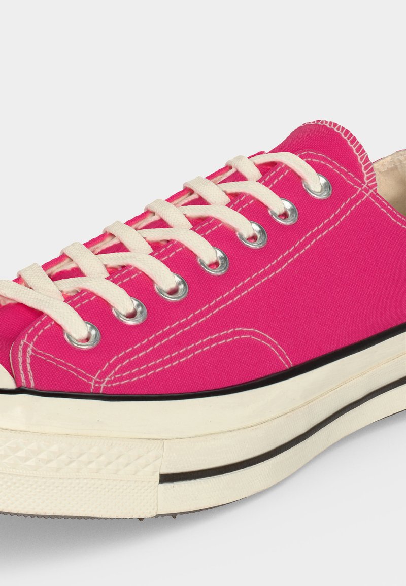 Knallpinker Canvas-Sneaker mit weißen Schnürsenkeln, Metallösen, weißen Nähten und einer dicken weißen Gummisohle mit schwarzer Umrandung.