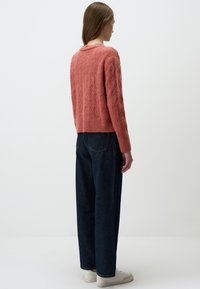 Maglione rosa lavorato a maglia con motivi a diamante testurizzati, scollatura rotonda e orlo a coste. Indossato con jeans a vita alta blu scuro e sneakers bianche.