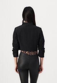 Svart kort jacka med långa ärmar och rynkning; har en midja med leopardmönster. Slät tyg och strukturerad design.