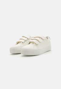 White sneakers with three Velcro straps, rubber sole, rounded toe, smooth leather upper, and a light blue accent on the heel.