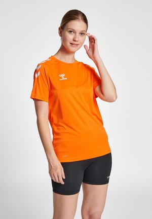 Lyst orange atletisk skjorte med korte ærmer, der har en rund halsudskæring og hvide logo detaljer. Sammen med sorte performance shorts.