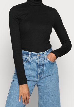 Schwarzes langärmeliges Rollkragenoberteil mit geripptem Muster, kombiniert mit hellblauen hochtaillierten Jeans im entspannten Schnitt und mit Vordertasche.