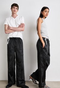 Gray ribbed tank top, white V-neck t-shirt, and black satin wide-leg pants with pockets and drawstring, paired with heeled sandals and boots.