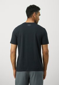 Black short-sleeve T-shirt with a smooth texture and logo at the back. Worn with gray athletic shorts, displayed from the back.