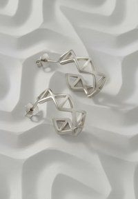 Silversmycken i geometrisk design med en zigzag-mönster och öppna triangulära former. Polerad metall med en elegant yta.